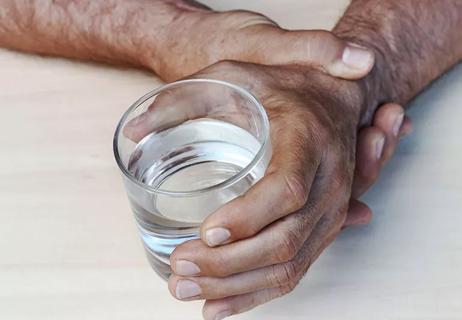 Close-up of a person trying to steady their trembling hand as they hold a glass of water