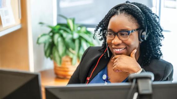 woman at desk with earphones smiling at computer screen