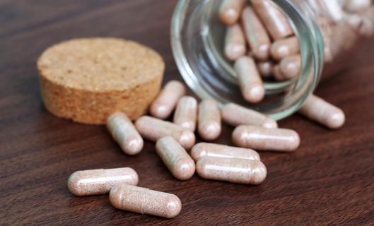 Capsules spilling out of a glass bottle with cork cap onto table