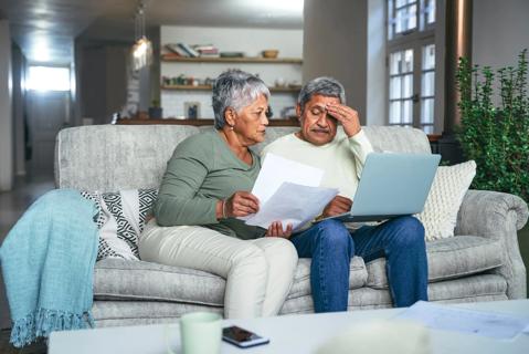 Woman holding papers while sitting on couch next to man with laptop computer