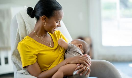 Smiling female looking down at baby while the baby breast feeds