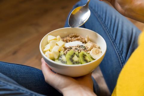 Person holding a bowl of fruits, nuts and oats on their lap