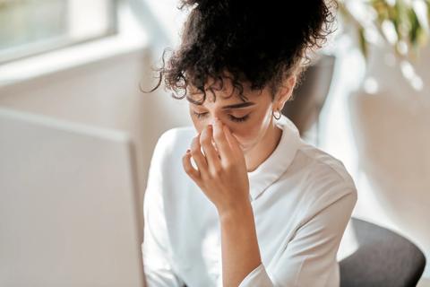 Person at work desk, head down, eyes closed and hand on bridge of nose