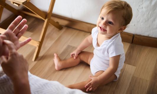Caretaker using baby sign language to communicate with baby sitting on floor