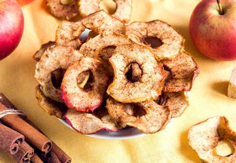 Homemade cinnamon apple chips in a white bowl on a yellow tablecloth, viewed from above.