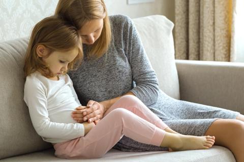 Child with mom sitting on couch with hands on the child's stomach