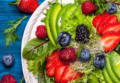 A plate of high-fiber fruits include strawberries, raspberries, blackberries and blueberries on a bed of lettuce and avocado.
