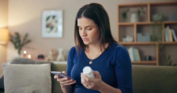Pregnant woman holding bottle of medication while researching it on her phone