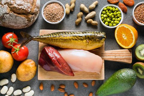 Stone table with niacin-rich foods, like nuts, avocado, tomatoes, and cutting board with raw liver, chicken and fish