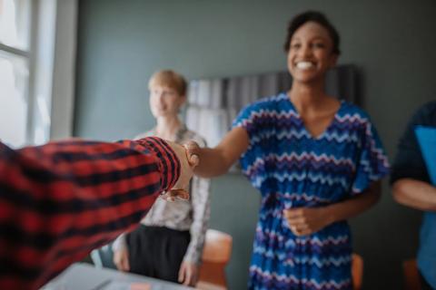 People standing, shaking hands across table from each other