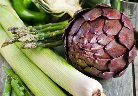 Stalks of celery, asparagus and artichoke sit on a wooden table.