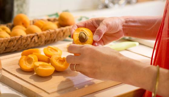 Person halving apricots and removing pits on cutting board