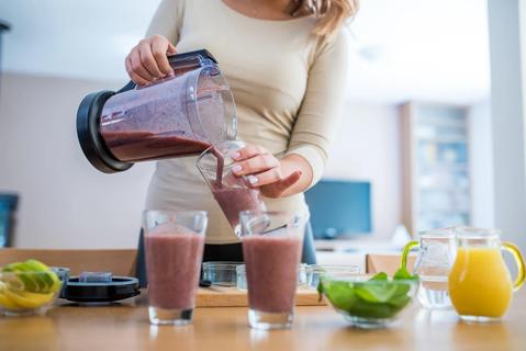 Person pouring freshly made smoothies from a blender into glasses