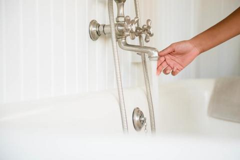 Hand testing water temperature from bathtub faucet