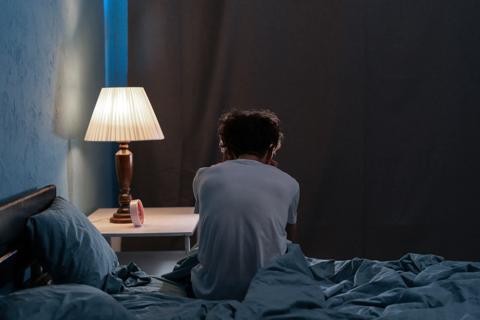 Person sitting on edge of bed at night, with bedside light on