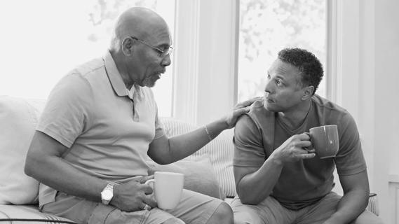Senior father and son talking while having coffee on sofa