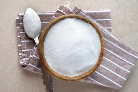 Artificial sweetener in wooden bowl on kitchen towel, with spoonful nearby