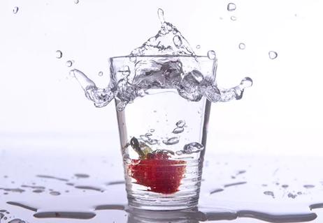 Glass of water splashing with a strawberry in it