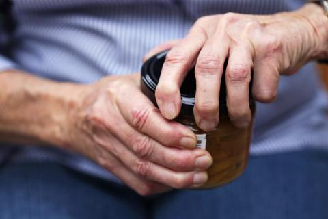 Close up of hands with swollen joints twisting a lid off a jar.