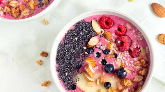 Bowl with raspberries, blueberries apples, almonds and chia seeds on a white tabletop