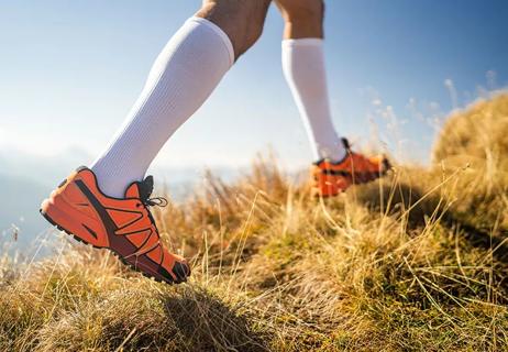 A runner on a grassy hill wearing orange sneakers and white knee-length compression socks