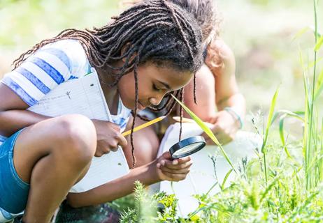 Girls examining plants outside during summer school class