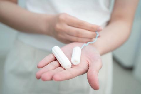 Hand holding two open, unused cotton tampons