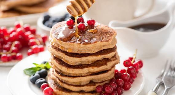 Stack of wheat and oatmeal pancakes on plate, with syrup drizzling over, with berries