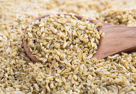 A wooden spoon sifts through a pile of uncooked freekeh