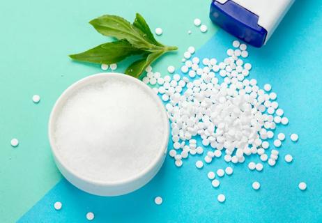 Closeup of sugar substitute in granulated and pill form on a blue background.