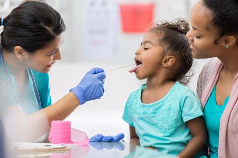 Toddler sitting on caregiver's lap receiving throat swab from healthcare provider