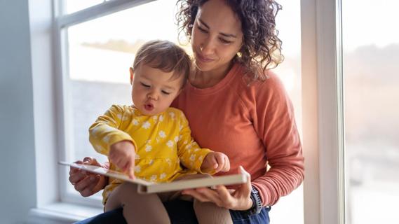 Caregiver and child read together in front of window