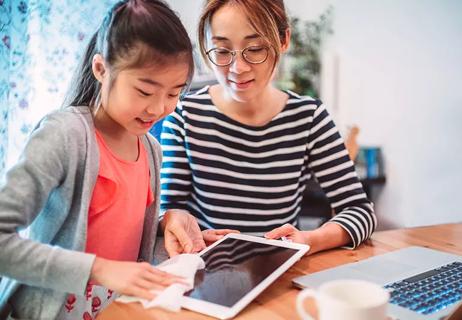 A woman watching a child clean her tablet with a cloth