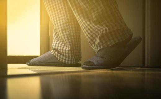 A person wearing blue plaid pajama bottoms and blue slippers walking toward the bathroom door.