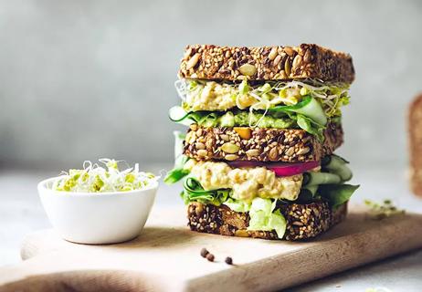 A double-decker sandwich made from multi-grain bread, sprouts, avocado, lettuce and tomato