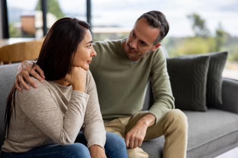 Two people sitting on couch, with one person comforting the other