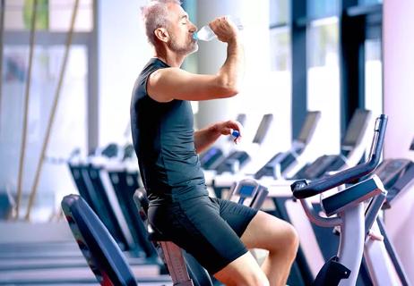 Person taking break on exercise bike to drink water, while at the gym.