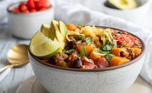 A bowl of chili with chunks of butternut squash, with lime wedge garnish