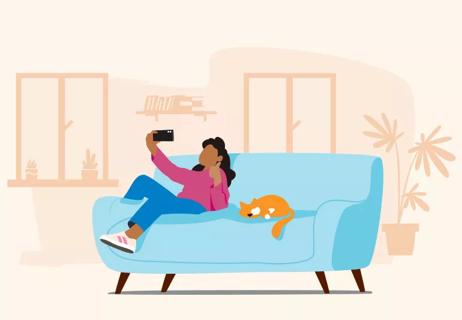Young teenager sitting on couch with cat while talking to friend on smartphone.