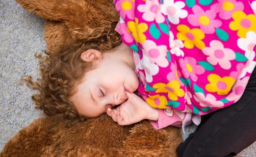Child lying down asleep, with thumb in their mouth