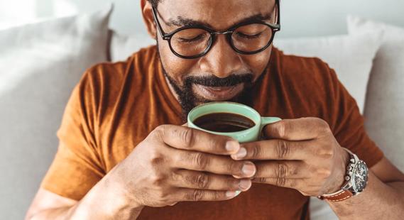 Happy person holding cup of coffee up to mouth, about to enjoy the drink