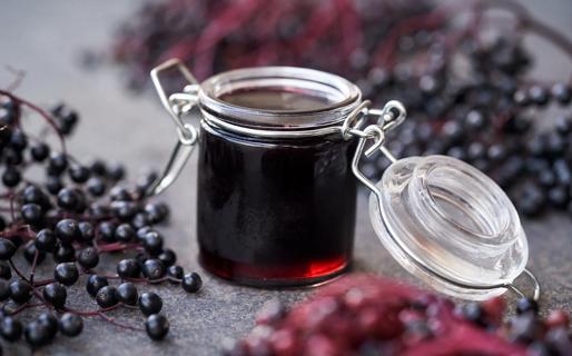 Jar of elderberry jam, with elderberry fruit nearby