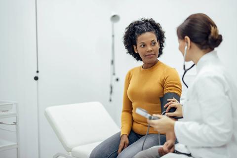 Person with blood pressure cuff on, having blood pressure read by healthcare provider