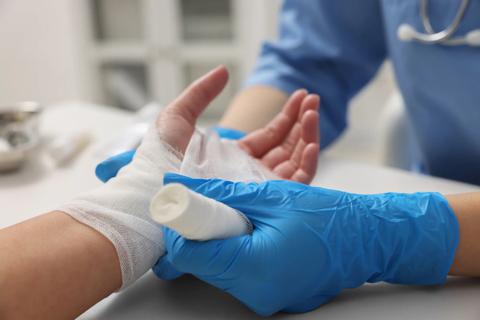 Hand being wrapped in gauze by healthcare provider wearing disposable medical gloves