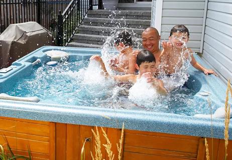Family enjoying the hot tub on their back porch wit younger boy splashing the water.