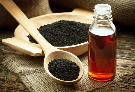 Black seed oil in bottle, with seeds in wooden spoon and bowl
