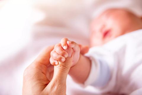 Newborn's tiny hand gripping caregiver's thumb