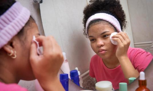 Teen looking in bathroom mirror, treating and cleaning their acne