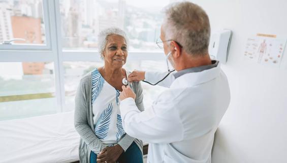 Healthcare provider listening to a patient's heart with stethoscope in exam room