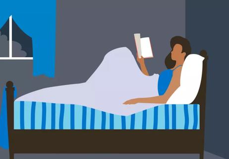 Person relaxes in bed reading before going to sleep at night.
